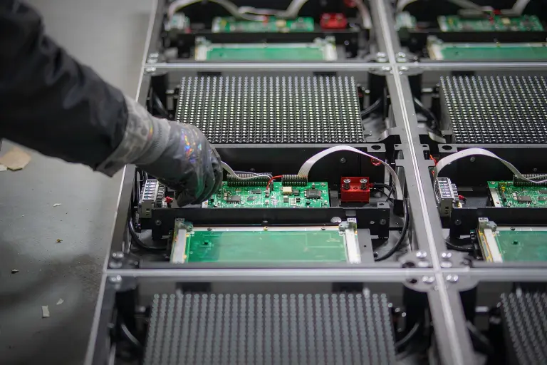 Technician servicing the modular cabinets and receiver cards behind an LED screen for advertising