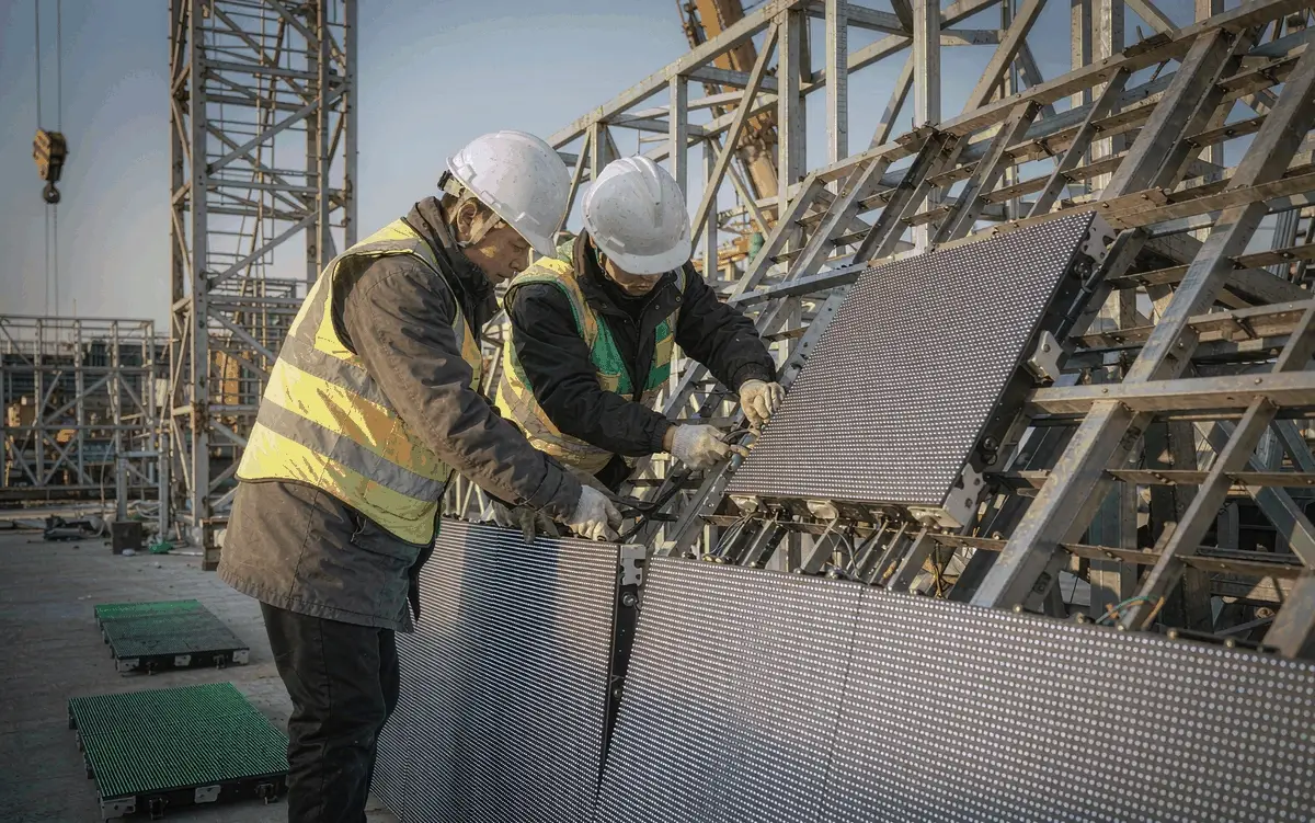 Engineers installing outdoor LED billboard modules onto a steel structure, one of the largest drivers of LED billboard cost